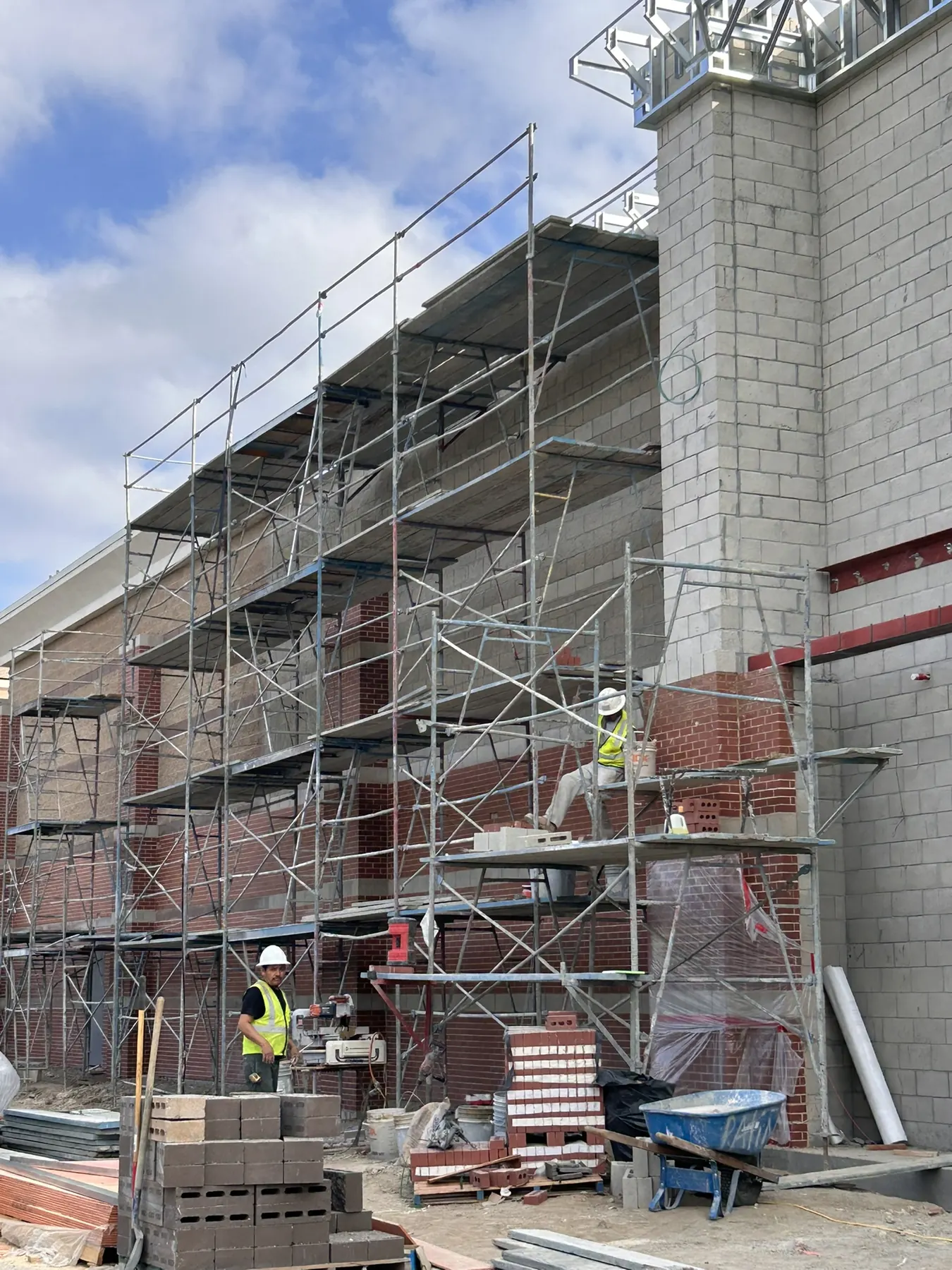 Masonry crew on scaffolding installing concrete block and brick veneer banding on a commercial building