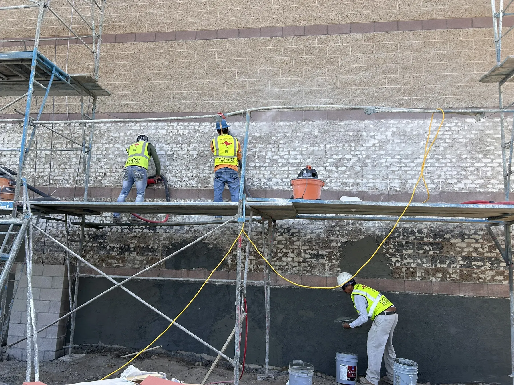 Masonry crew finishing a two-tone concrete block wall on a commercial building