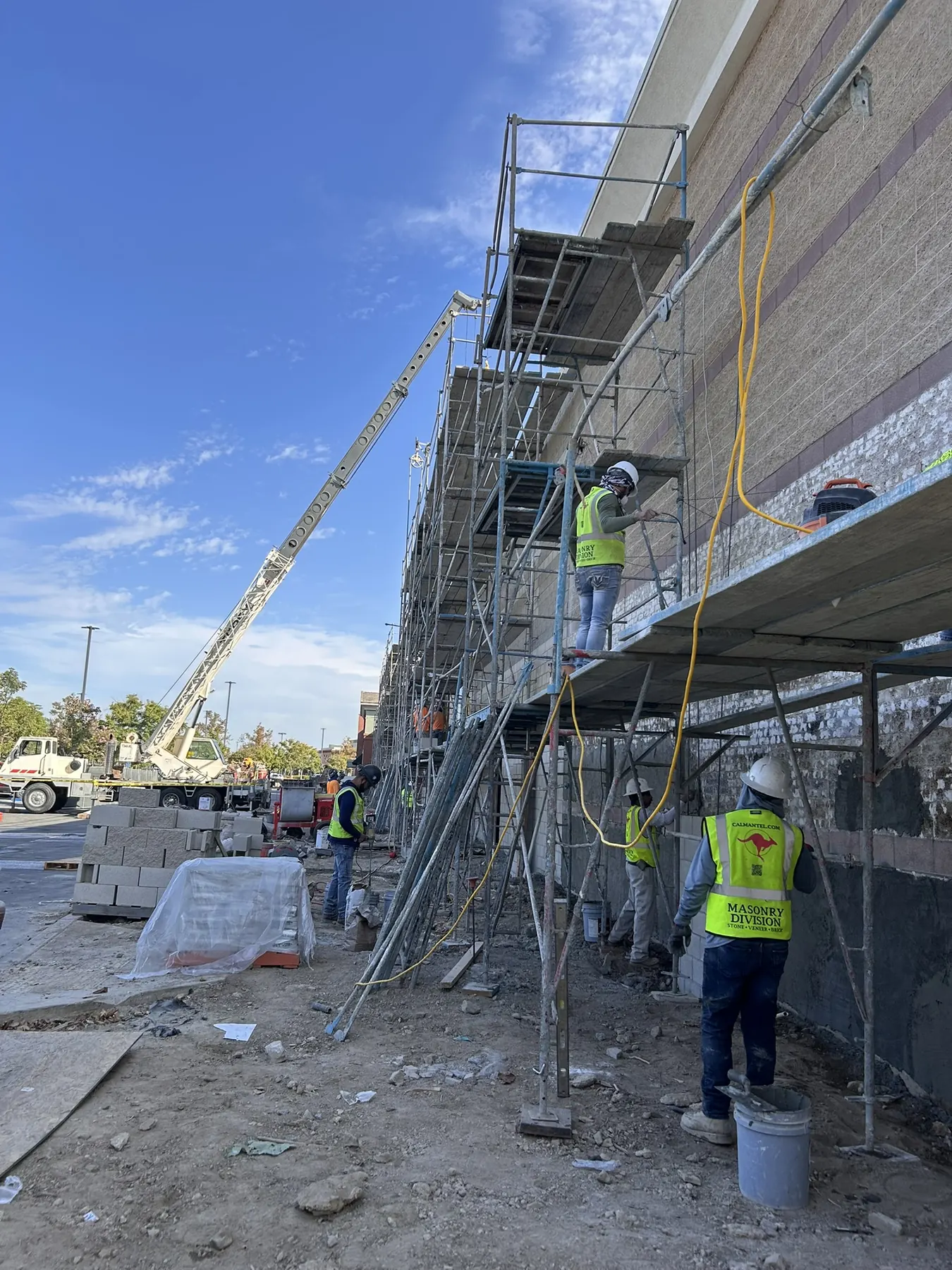 Masonry Division crew installing veneer on a commercial building exterior from scaffolding with a crane nearby