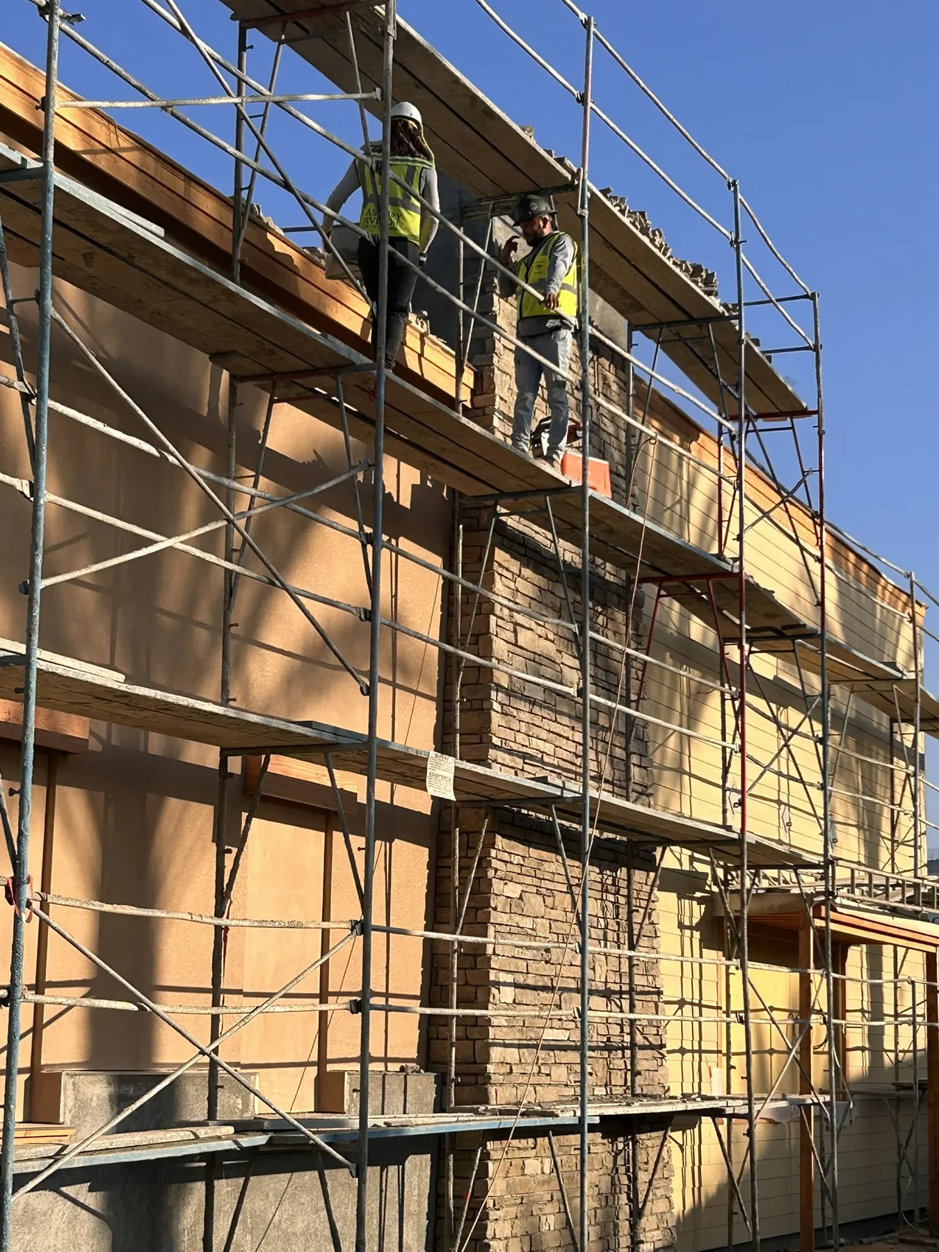 Masonry crew installing natural stone veneer piers on a multi-story building exterior