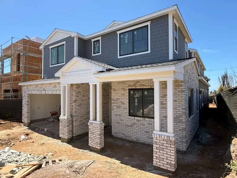 New two-story home with brick veneer entry columns and wainscot beneath gray shake-style siding