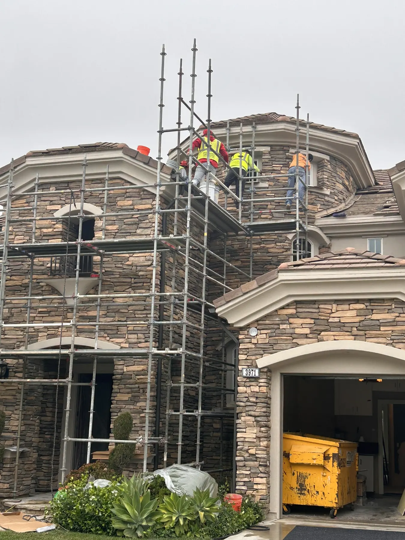 Masonry crew installing natural stone veneer on a large custom home exterior from scaffolding