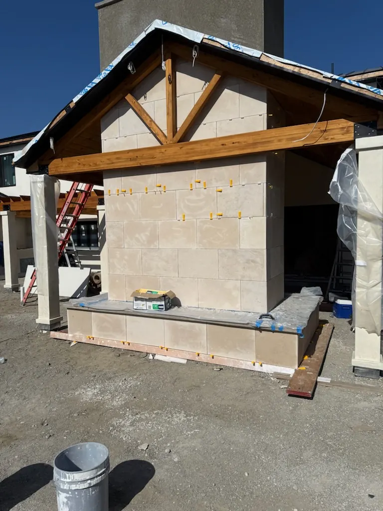 Outdoor cabana structure under construction with a stone veneer chimney and exposed wood beam roof