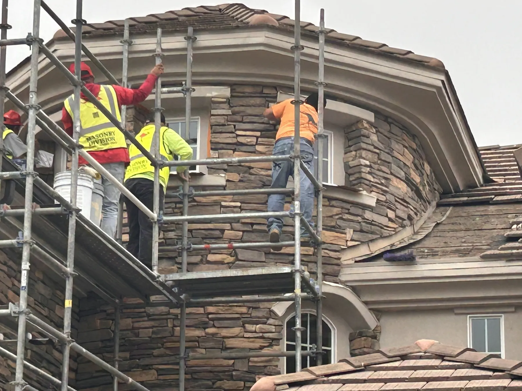 Masonry Division crew hand-setting natural stone veneer on a custom home's turret dormer
