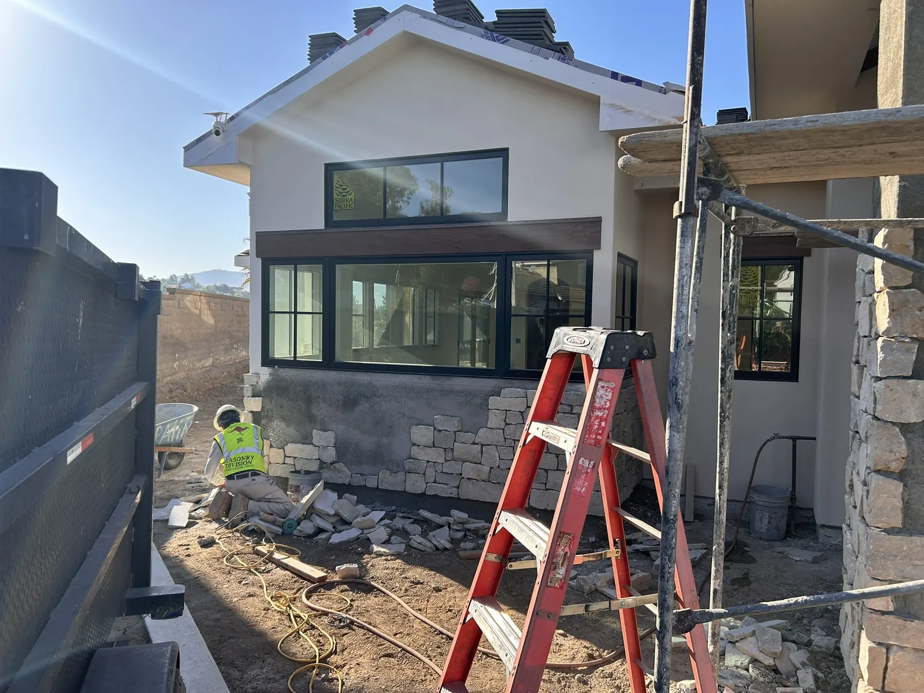 Masonry crew setting a stacked stone veneer wainscot base beneath large windows on a new home