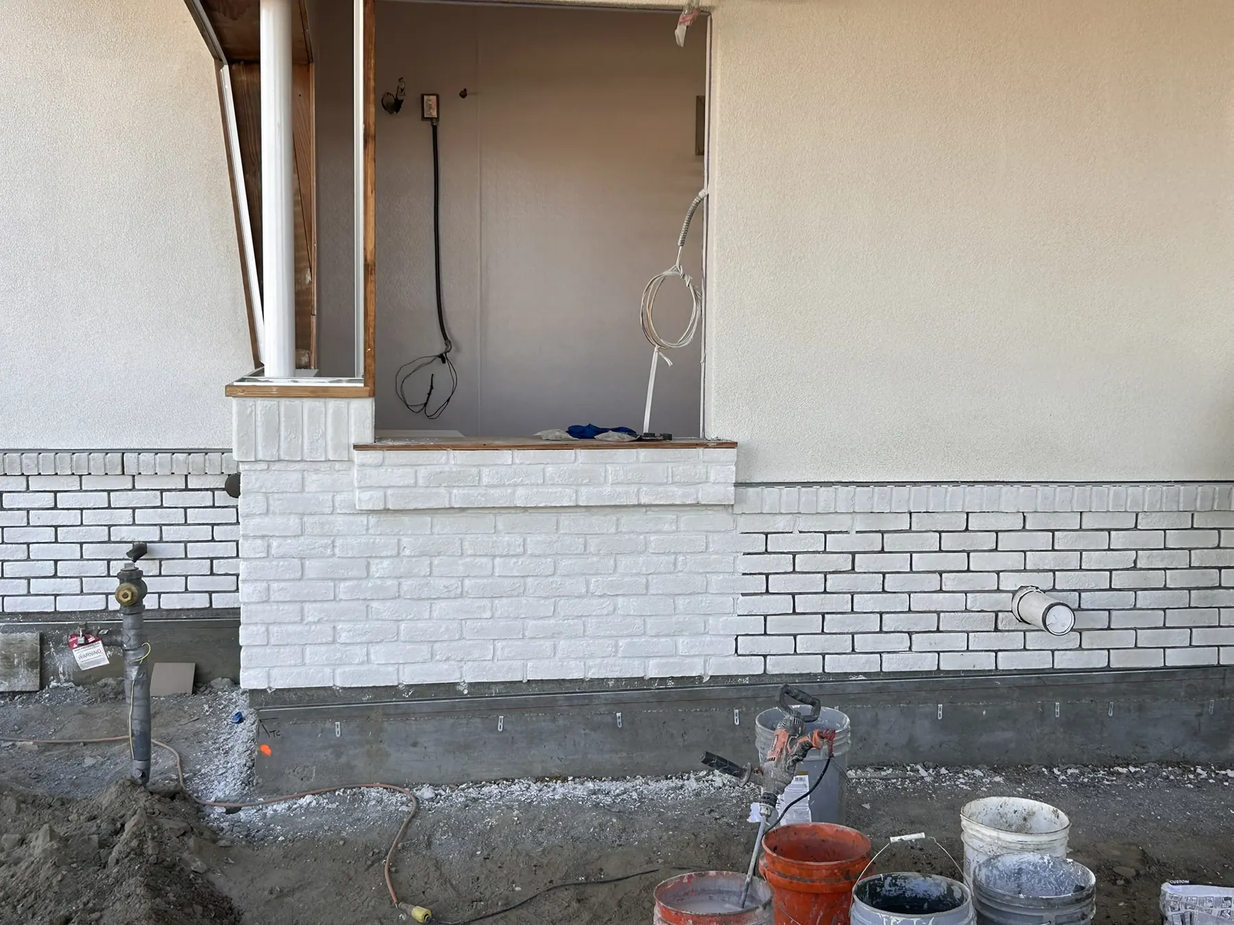 White brick veneer wainscot base installed along a stucco home exterior